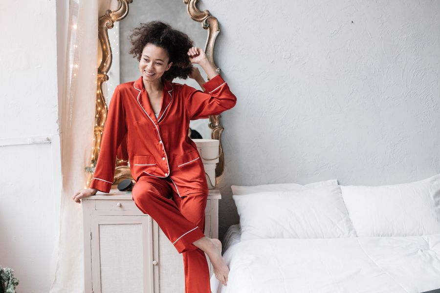 Woman in a pomegranate red night suit beside a mirror and a white bed